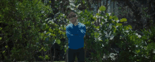 a man in a blue sweater is standing in a lush green forest