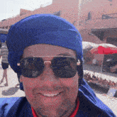a man wearing sunglasses and a blue turban has a reflection of a red umbrella in his sunglasses