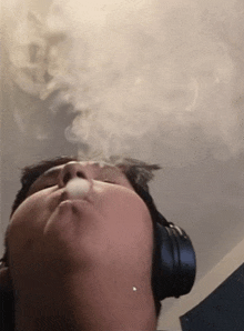 a man wearing headphones is smoking a cigarette and blowing smoke out of his mouth .