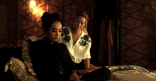 two women sitting on a bed with one wearing a white shirt with blue flowers on it
