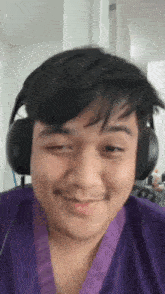 a young man wearing headphones and a purple robe is smiling .