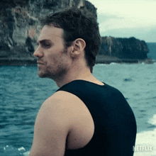 a man in a black tank top is sitting on a boat in the water .