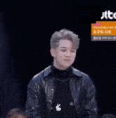 a man in a black leather jacket stands in front of a jtbc advertisement