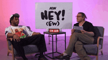 two people are sitting in front of a sign that says " hey "