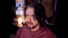 a man with a beard wearing headphones and a red shirt is sitting in front of a computer screen .
