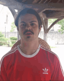a man wearing a red adidas shirt has a hat on his head