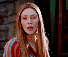 a woman with long red hair is making a funny face while wearing a striped shirt .