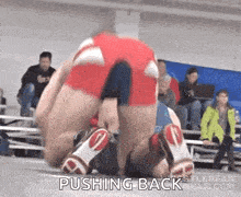 a wrestler is pushing back another wrestler on the mat .