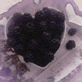 a heart shaped bowl filled with blackberries is on a table