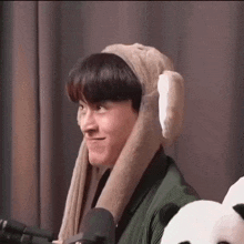a young man wearing a bunny hat is sitting in front of a microphone and making a funny face .