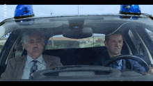 two men are sitting in a police car with a blue light on top of the car