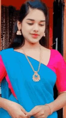 a young woman wearing a blue saree and a pink blouse is standing in front of a door .