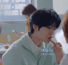 a man in a green jacket is eating a piece of food with korean writing on it