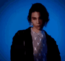 a man in a black jacket is standing in front of a blue background
