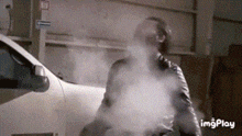 a man standing in front of a white car with smoke coming out of his mouth .