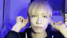 a person with blonde hair is covering their ears with their hands