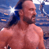 a shirtless wrestler with a beard and long hair stands in front of a crowd in a stadium