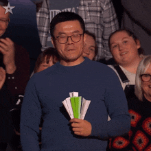 a man in a blue sweater is holding a fan in front of a group of people