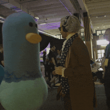 a blue stuffed bird with a yellow beak is standing in a crowded room