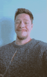 a man with a beard wearing a grey sweater makes a funny face