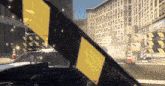 a black car is driving down a street with a yellow and black striped barrier