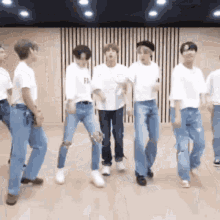 a group of men in white shirts and blue jeans are dancing in a room .