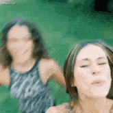 two women are standing next to each other in the grass .
