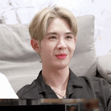a young man with blonde hair is sitting on a couch wearing a black shirt