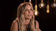 a woman with long blonde hair is making a funny face in a dark room with lights hanging from the ceiling .
