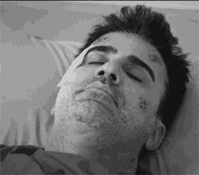 a black and white photo of a man laying in a hospital bed with a bandage on his face .