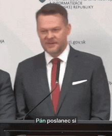 a man in a suit and tie is standing at a podium with a sign that says pan poslanec si