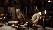 a woman in a blue shirt with the letter g on it stands in front of a cake