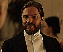 a man with a beard is wearing a black tuxedo and white bow tie
