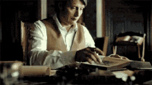 a man is sitting at a table with a book in his hands .