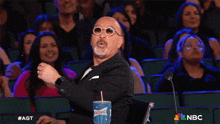 a bald man sitting in front of a crowd with a sonic drink in his hand
