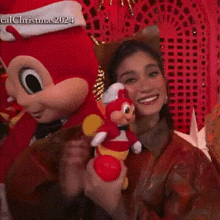 a woman is holding a stuffed animal and smiling while standing next to a mickey mouse mascot .