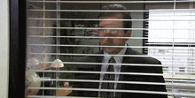 a man in a suit and tie is looking out of a window through blinds