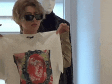 a man wearing sunglasses is holding a t-shirt in front of a mannequin in a store .