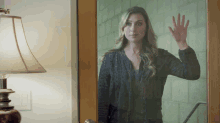 a woman in a black jacket waves her hand through a glass door