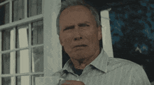 an older man in a striped shirt is standing in front of a door holding a cup of coffee .