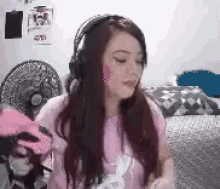a woman wearing headphones and a pink shirt is sitting in front of a fan .