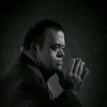 a man with down syndrome is wearing a suit and tie and praying with his hands together in a black and white photo .