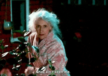 a woman in a pink robe is standing next to a plant and talking .