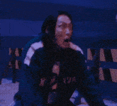 a woman in a blue jacket is kneeling down in a dark room while a man holds her hand .