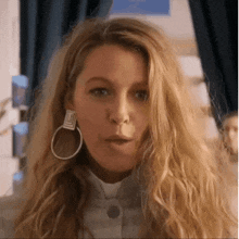 a woman wearing hoop earrings and a white shirt is making a funny face .