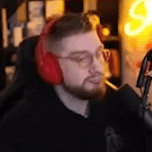 a man with a beard is wearing headphones and smoking a cigarette in front of a microphone .