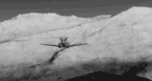 a black and white photo of a plane flying through the clouds over a mountain .