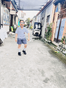 a little boy in a school uniform is walking down a street with a tricycle in the background