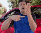a man in a blue shirt is pointing at something while standing in front of a red truck