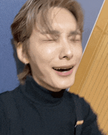 a man wearing a black turtleneck is making a funny face with his eyes closed